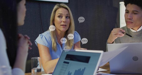 Speaking center blonde woman in blue blouse responding at meeting table, laptop chart speech icons