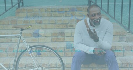 Sitting man speaking into smartphone on brick steps, with bicycle, charts, gray sweater, copy space