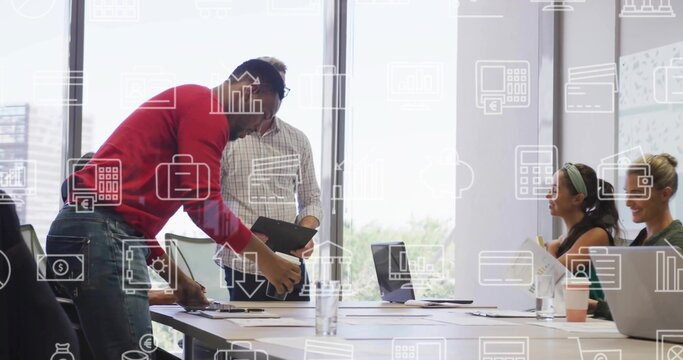 Arranging papers, man in red sweater leaning over office table with laptops, tablet, docs, icons