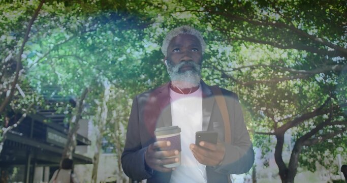 Standing midadult man wearing blazer white shirt on tree-lined walk, checking phone, holding coffee