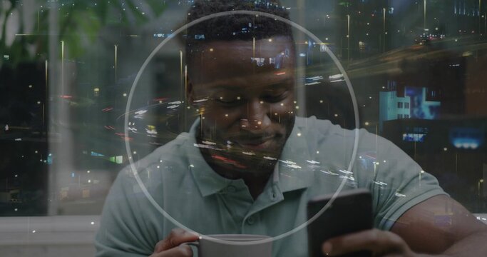 Holding mug, man checking smartphone at table next to window, wearing polo, circular reflection