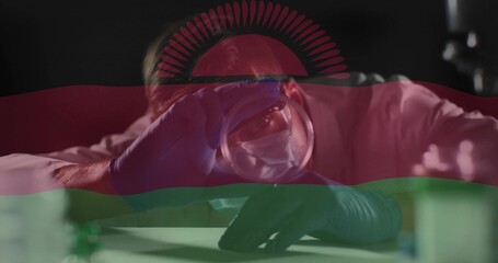 Leaning scientist holding glass sphere to eye at lab bench, white coat, blue gloves, flag overlay