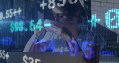 Sipping woman in short-sleeve top leaning toward laptop at desk, holding mug with ticker graphics