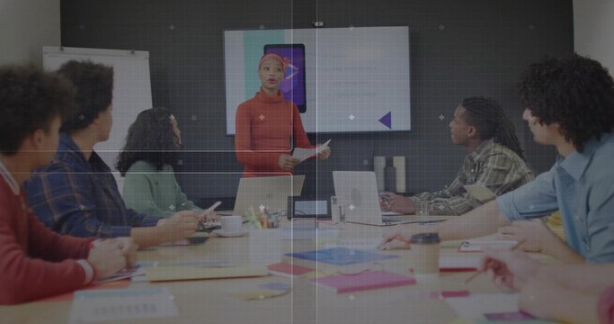 Presenting woman in red sweater and headwrap speaking in conference room, with screen and laptops