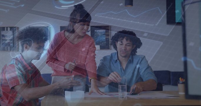Reviewing project team leaning over printed charts at meeting table, coral sweater and plaid shirt