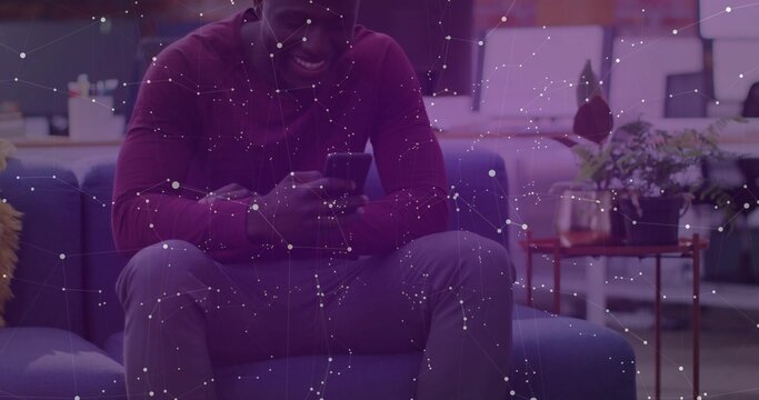 Sitting African American man wearing maroon shirt and watch, checking smartphone on sofa in lounge
