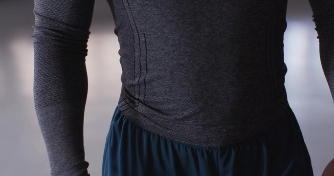 Standing dancer wearing fitted gray top and loose blue trousers in studio, reflective floor - Powered by Adobe