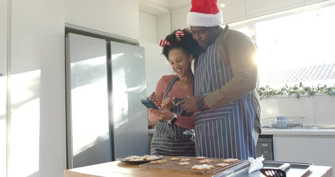 Diverse couple checking timer for cookies and guiding tapping on smartphone at kitchen island