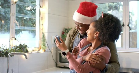 Diverse couple wearing aprons scrolling smartphone in home kitchen while laughing over surprise - Powered by Adobe