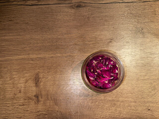 Glass jar with tea rose petals on a wooden surface, top view, soft light, copy space. Elegant, minimalistic background for spa, wellness designs, cooking themes, herbal cosmetics, self-care projects