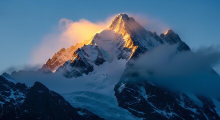 A majestic snow-capped mountain peak is illuminated by a golden glow from the sun, with clouds whisked around the summit