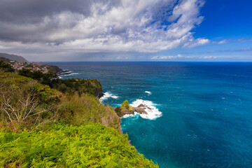Dramatic Waves and Coastal Village Beneath Towering Cliffs, Madeira island, Portugal, background or travel wallpaper