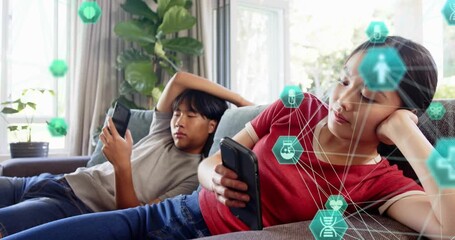 Man reclining, woman scrolling on couch, tapping phones and activating teal health icons around her - Powered by Adobe