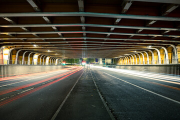A symmetric, long exposure photograph of a roadway passing through a low-lit, vaulted tunnel, showcasing the light trails from vehicle traffic in both directions.