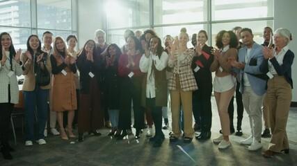 Group of happy business professionals stand together, clapping enthusiastically after a successful presentation. Their positive energy fills the conference room, showing appreciation and celebration.