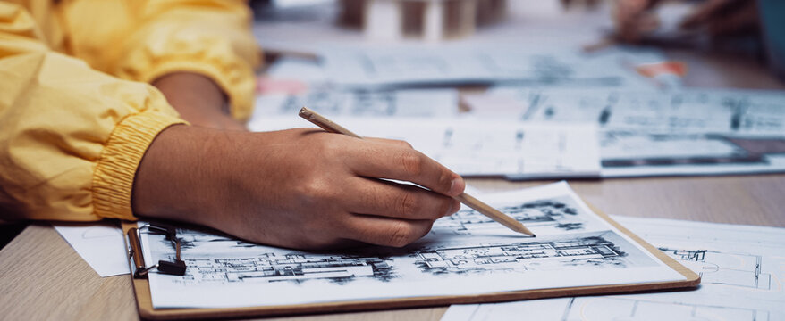 A young architect is focused on sketching building plans on paper with a pencil. The scene highlights the vibrant atmosphere of collaboration and creativity in a design workspace. SACTR - Powered by Adobe