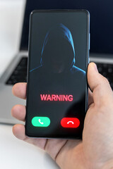 Hand Holding a Smartphone Displaying a Critical Digital Warning Call from an Anonymous Hooded Cyber Hacker Figure