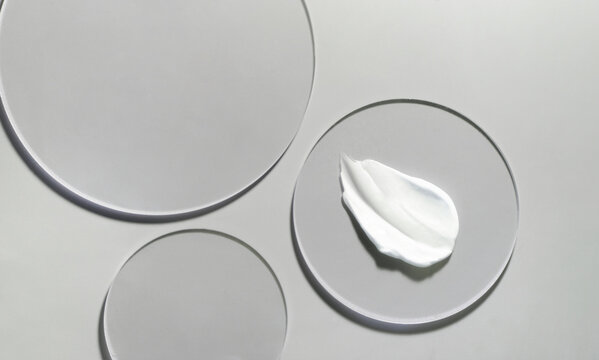 Beauty product flat lay mock up swatch on glass circle stands on grey backdrop. White skin care cream
