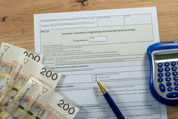 Blue calculator with PIT-37 tax form and 200 Polish zloty banknotes, personal finance and accounting concept