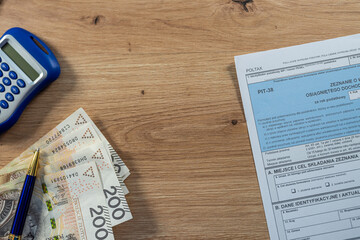 Blue calculator with PIT-38 tax form and Polish 200 zloty bills, investment income and capital gain concept