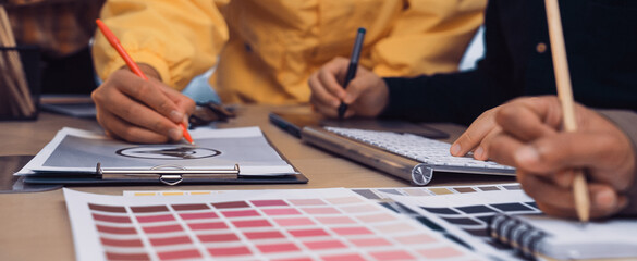 A diverse team of professionals actively collaborates on a design project, using color swatches and sketches in a modern office environment, showcasing creativity and teamwork. SACTR