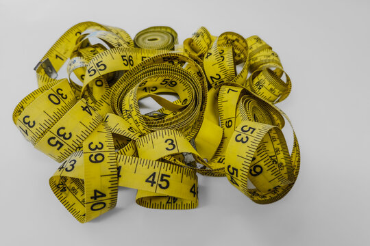 A pile of yellow, flexible measuring tapes with black imperial and metric markings isolated on a white background.