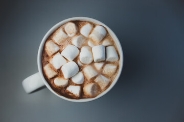 A warm mug of rich, creamy hot chocolate topped with a generous layer of fluffy marshmallows isolated on a table surface. high angle perspective with copy space flat lay background
