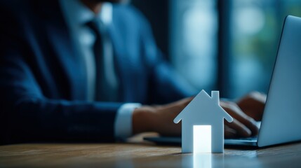 Businessman Working on Laptop with Small House Model and Modern Office Background Showing Real Estate and Financial Concepts