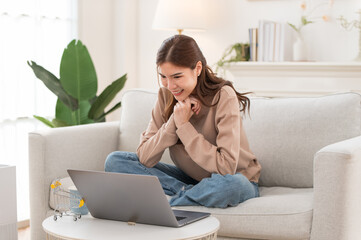 Concentrated Asian girl sit on couch working on laptop browsing internet at home, young woman busy using computer surfing wireless web shopping online