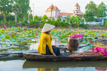 Vietnamese woman rowing a wooden boat harvesting water lilies in the Mekong Delta