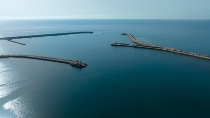 Aerial view of the mouth of a port. The sea extends to the horizon in a backlight.