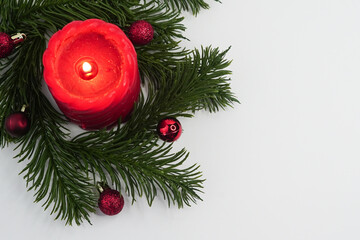 Red Candle with Christmas Tree Branches and Ornaments on White Background