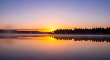Obraz premium Calm lake reflecting the sunrise with trees and fog in the distance at a peaceful morning scene