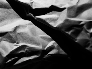 Crumpled black and white paper with deep creases and folds, creating a textured and jagged surface. 