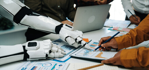 A unique business meeting scene where human and robot collaborate on data analysis, showcasing technology integration in modern workspace dynamics.Noogenesis