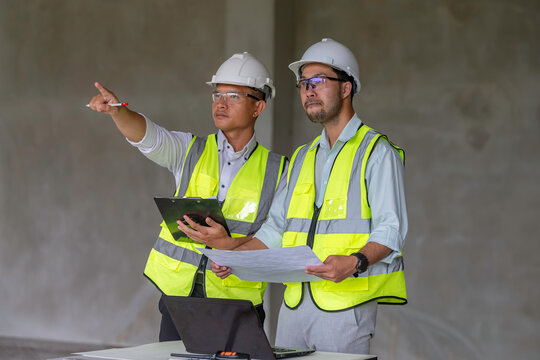 Two engineers discussing architectural blueprints at a construction site, representing planning, teamwork, safety, and engineering project management in a real-world industrial environment.