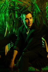 Fashionably dressed gentleman stares at vibrant plant life scene behind him