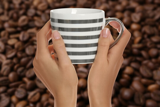 Woman holding striped cup against roasted coffee beans, closeup