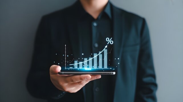 Businessman's hand holding a smartphone displaying a glowing financial growth chart with percentage symbol.