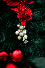 Festive Christmas decorations featuring shimmering golden berries and a vibrant red ornamental flower nestled among deep green pine branches. The warm, elegant holiday atmosphere. Close-up.