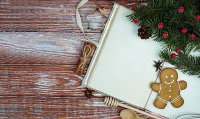 Festive flatlay composition with vintage old recipe book, Christmas decorations, gingerbread cookie, pine branches, cinnamon and baking tools on a rustic wooden background. Holiday recipes. Top view.