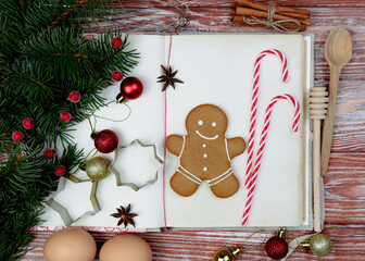 Christmas festive flatlay composition with vintage old recipe book, gingerbread man and Christmas decorations on the wooden background. Homemade holiday baking. Close-up. Selective focus.