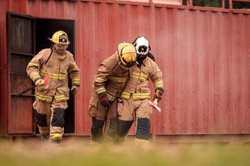 A team of firefighters evacuates an injured colleague from a smoke-filled training structure