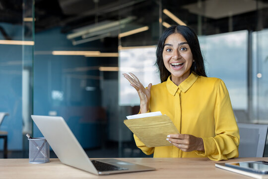 Portrait of a young Indian woman in the office, holding an open letter in her hands, smiling and looking at the camera