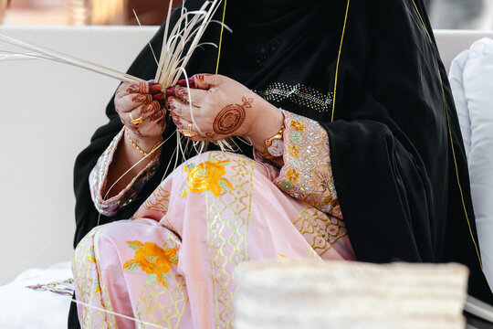 Emirati woman artisan weaving traditional Al Khous from dried palm leaves, closeup on hands. UAE heritage and sustainable craft concept.