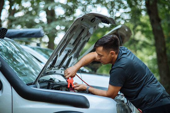 Man Jump-Starting Car in Nature with Jumper Cables.