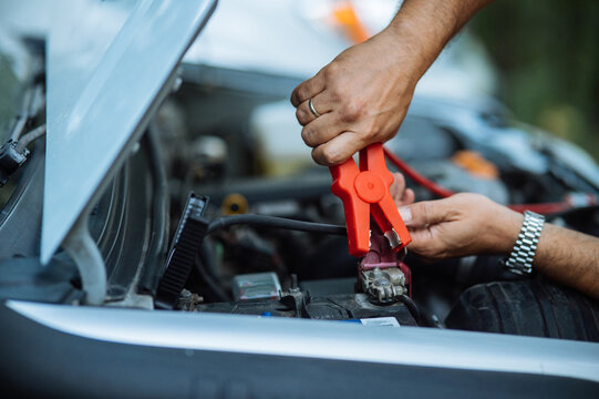 Person Jumpstarting a Car with Battery Cables. Close up of hands.