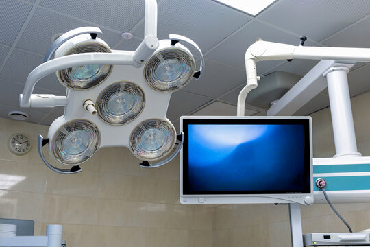 A medical operating room with a large monitor displaying a blue image