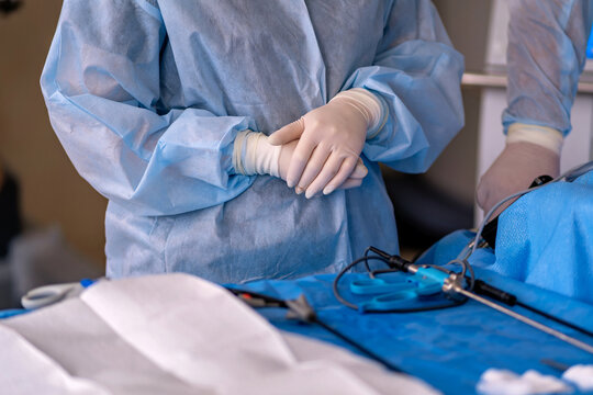 A surgeon in a blue scrub suit and white gloves is holding the hand of another surgeon