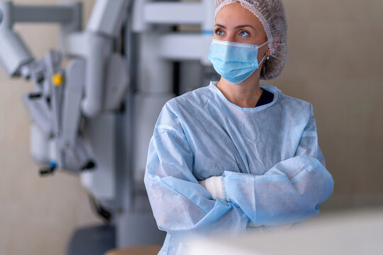 A woman in scrubs and a mask standing in front of an operating room - Powered by Adobe